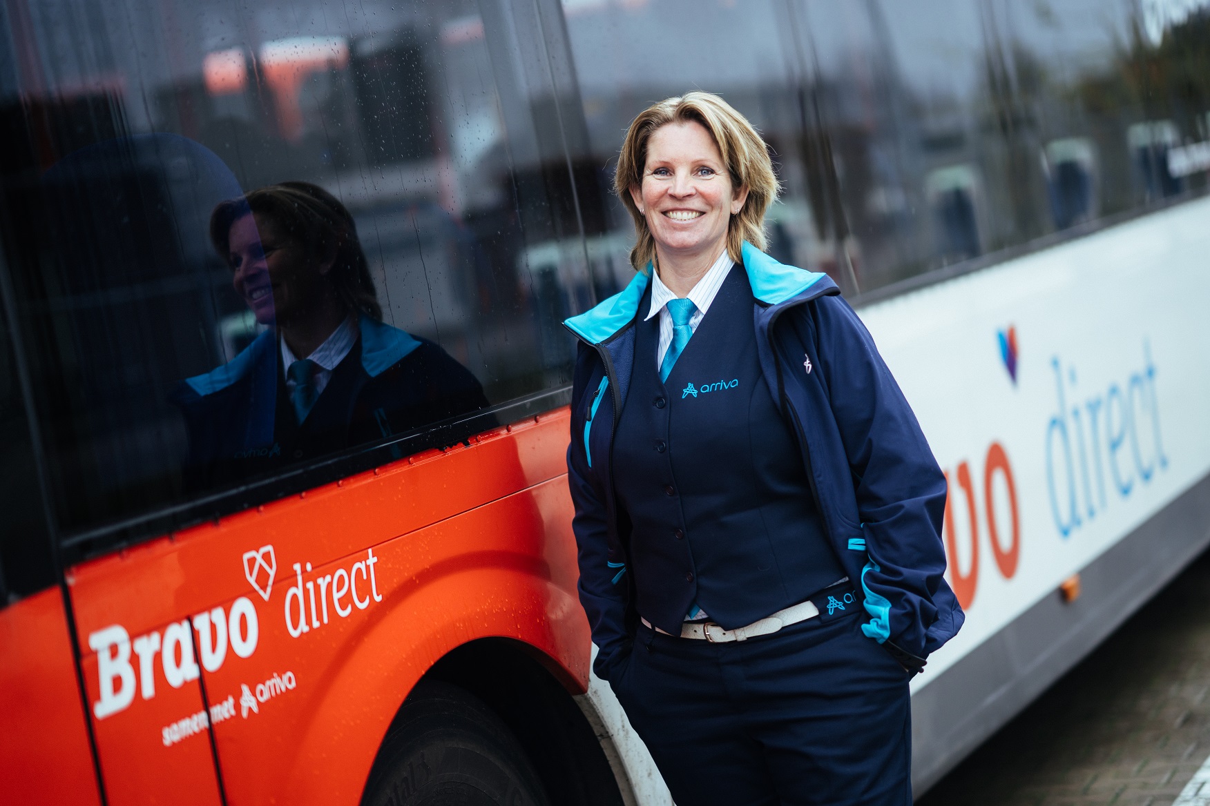 Buschauffeur Katja staat lachend naast haar Arriva-bus.
