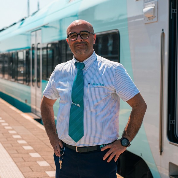 Een lachende machinist in Arriva-uniform staat voor de trein en kijkt in de camera. Een lachende machinist in Arriva-uniform staat voor de trein en kijkt in de camera.