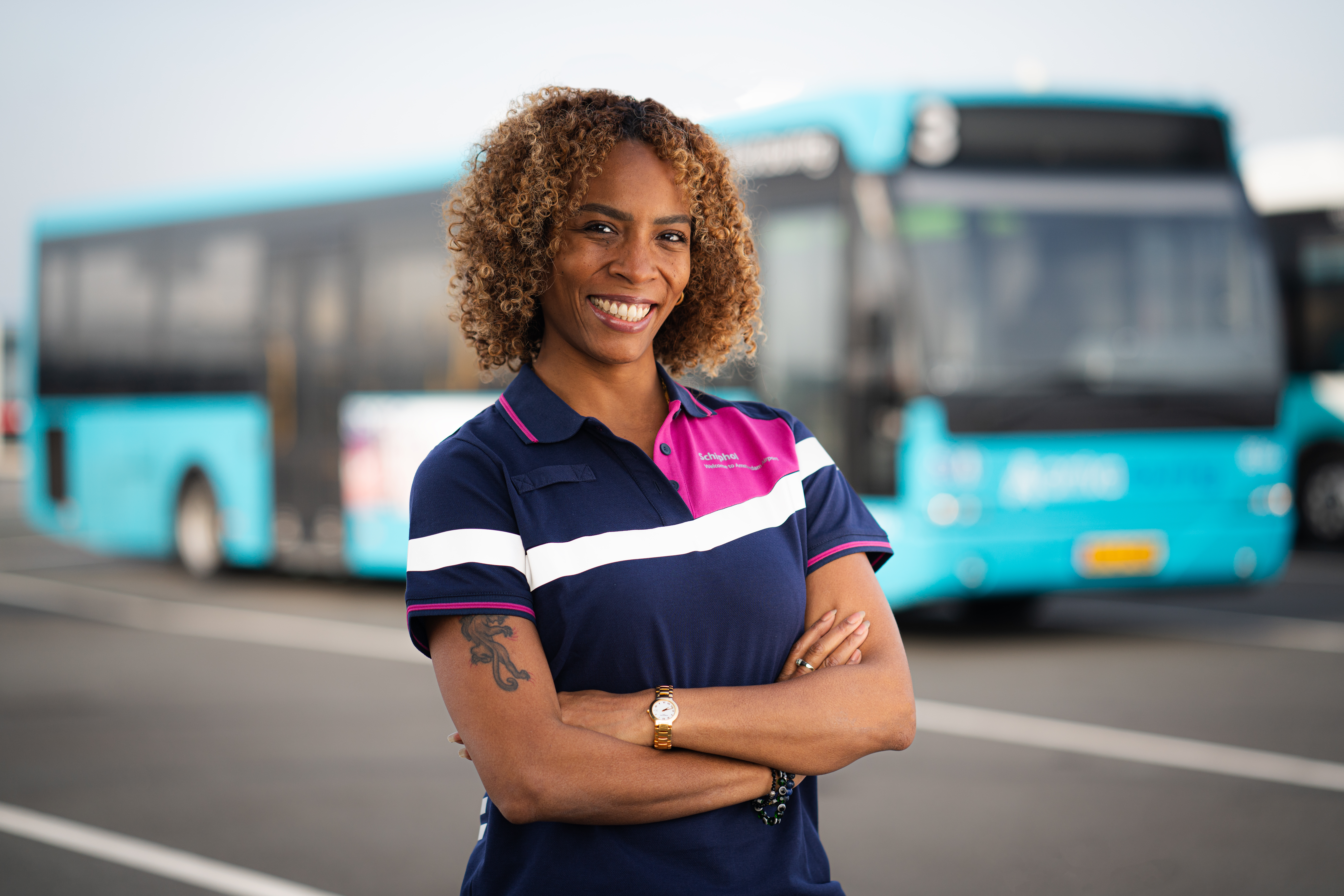 Chauffeur van Arriva in Schiphol-uniform staat met haar armen over elkaar en lacht naar de camera.