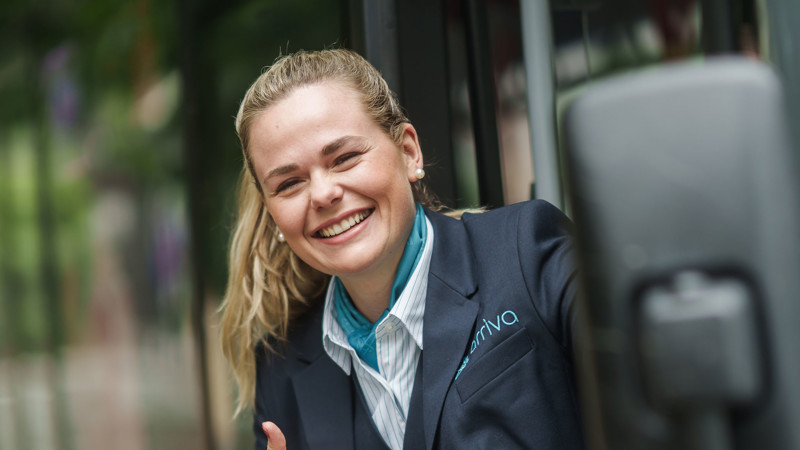 Een lachende buschauffeur van Arriva in uniform steekt haar duim op en lacht breed terwijl ze uit de bus stapt. Een lachende buschauffeur van Arriva in uniform steekt haar duim op en lacht breed terwijl ze uit de bus stapt.