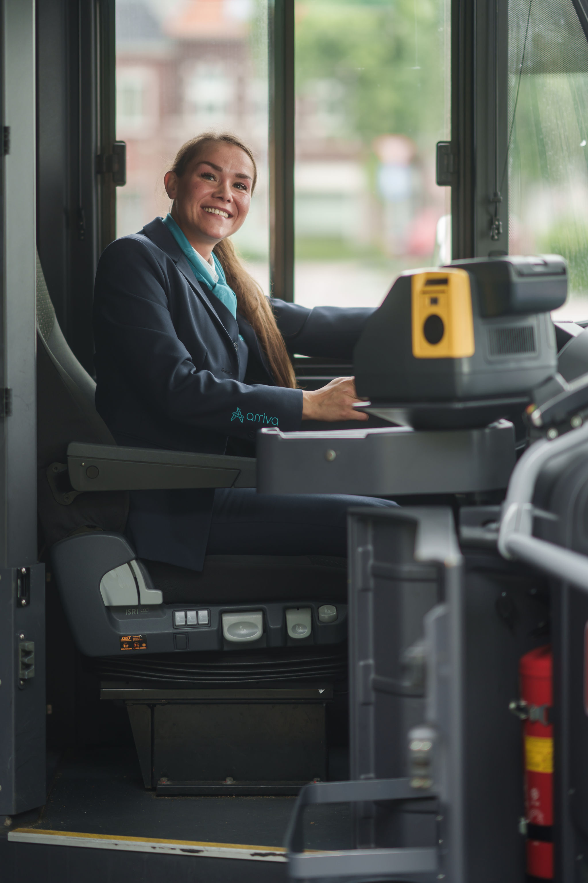 Een chauffeur van Arriva zit achter het stuur van haar bus en kijkt lachend richting de ingang van haar bus.