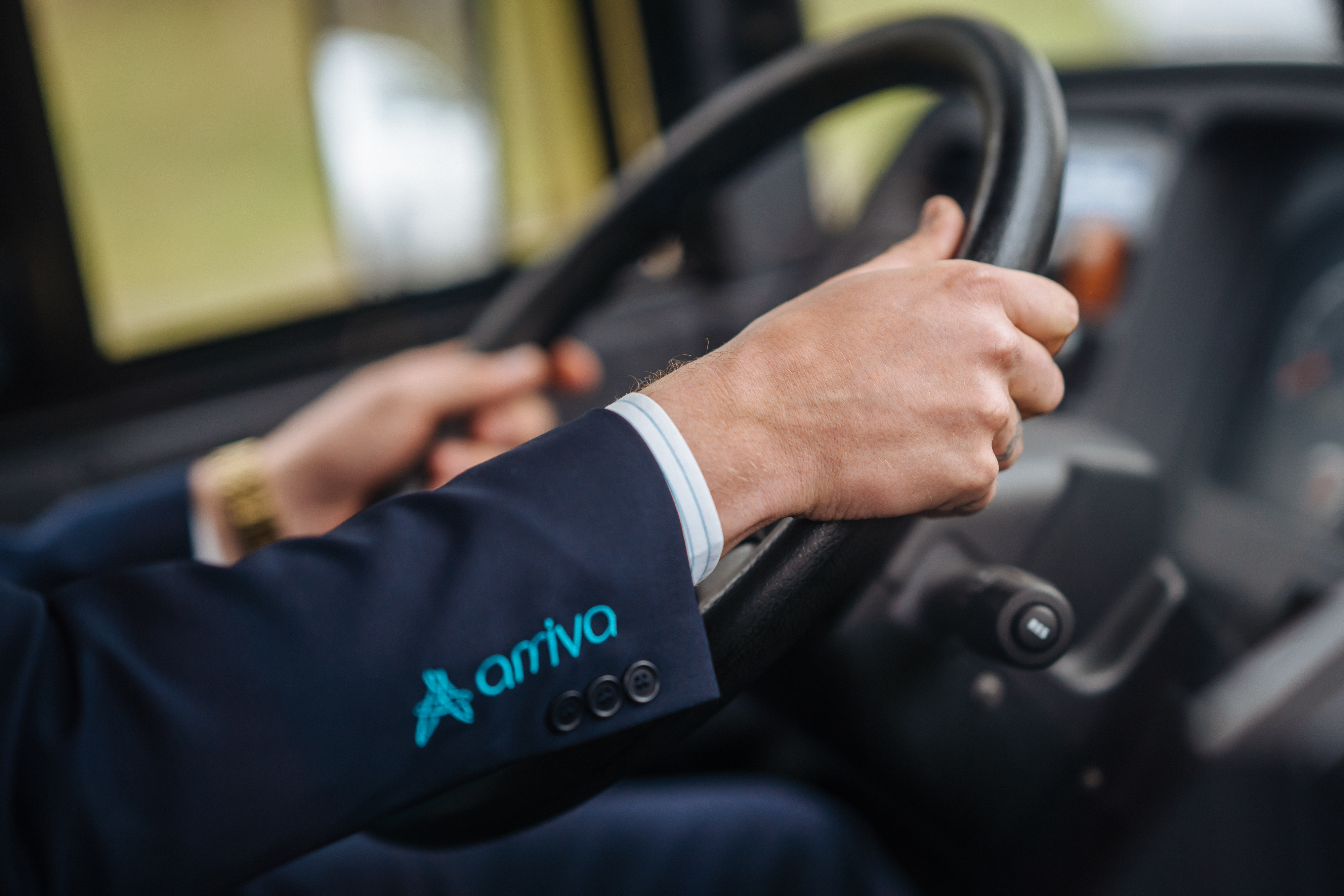 De handen van een buschauffeur aan het stuur van zijn bus, er is nog 'Arriva' te zien op de mouw van zijn jasje.