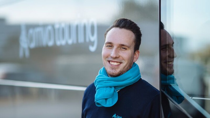 Touringcarchauffeur Benjaming staat lachend naast zijn touringcar. Touringcarchauffeur Benjaming staat lachend naast zijn touringcar.