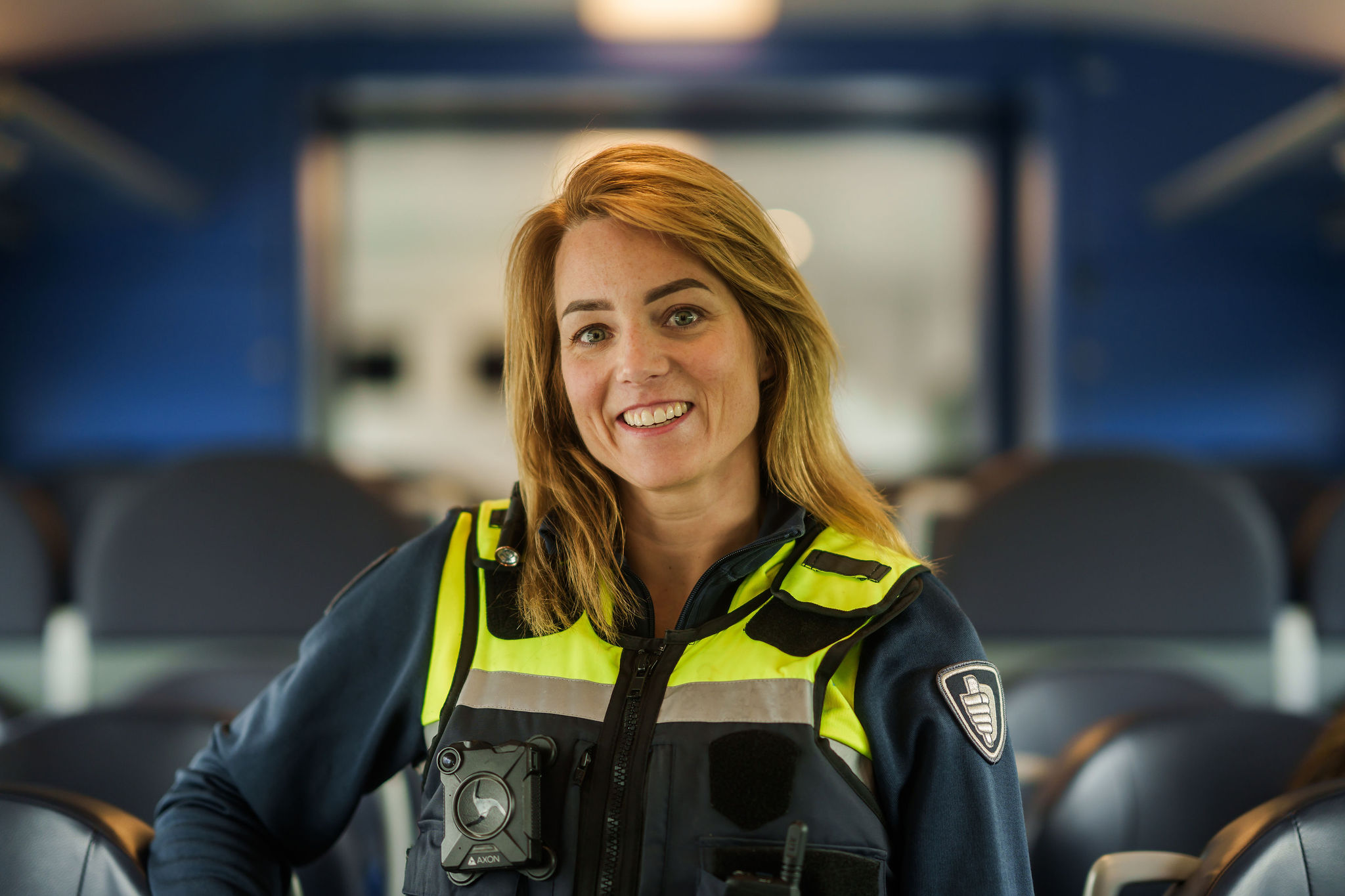 Medewerker service & veiligheid van Arriva staat in haar uniform in een trein tussen de stoelen en lacht.