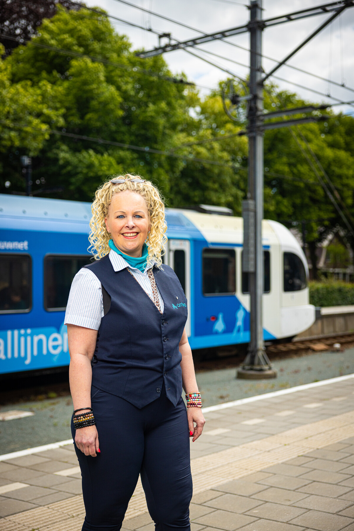 Een lachende Steward BOA-OV staat bij een trein van Arriva.