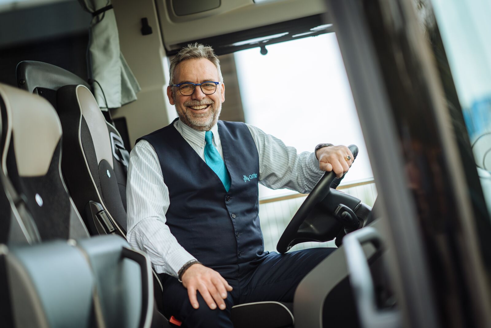 Chauffeur zit achter het stuur van een Arriva touringcar en lacht.