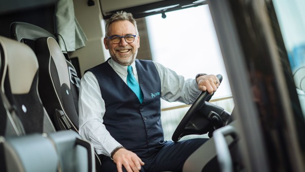 Chauffeur zit achter het stuur van een Arriva touringcar en lacht. Chauffeur zit achter het stuur van een Arriva touringcar en lacht.