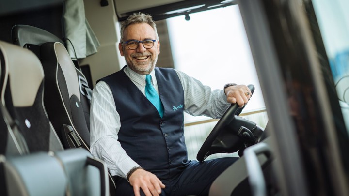 Chauffeur zit achter het stuur van een Arriva touringcar en lacht. Chauffeur zit achter het stuur van een Arriva touringcar en lacht.