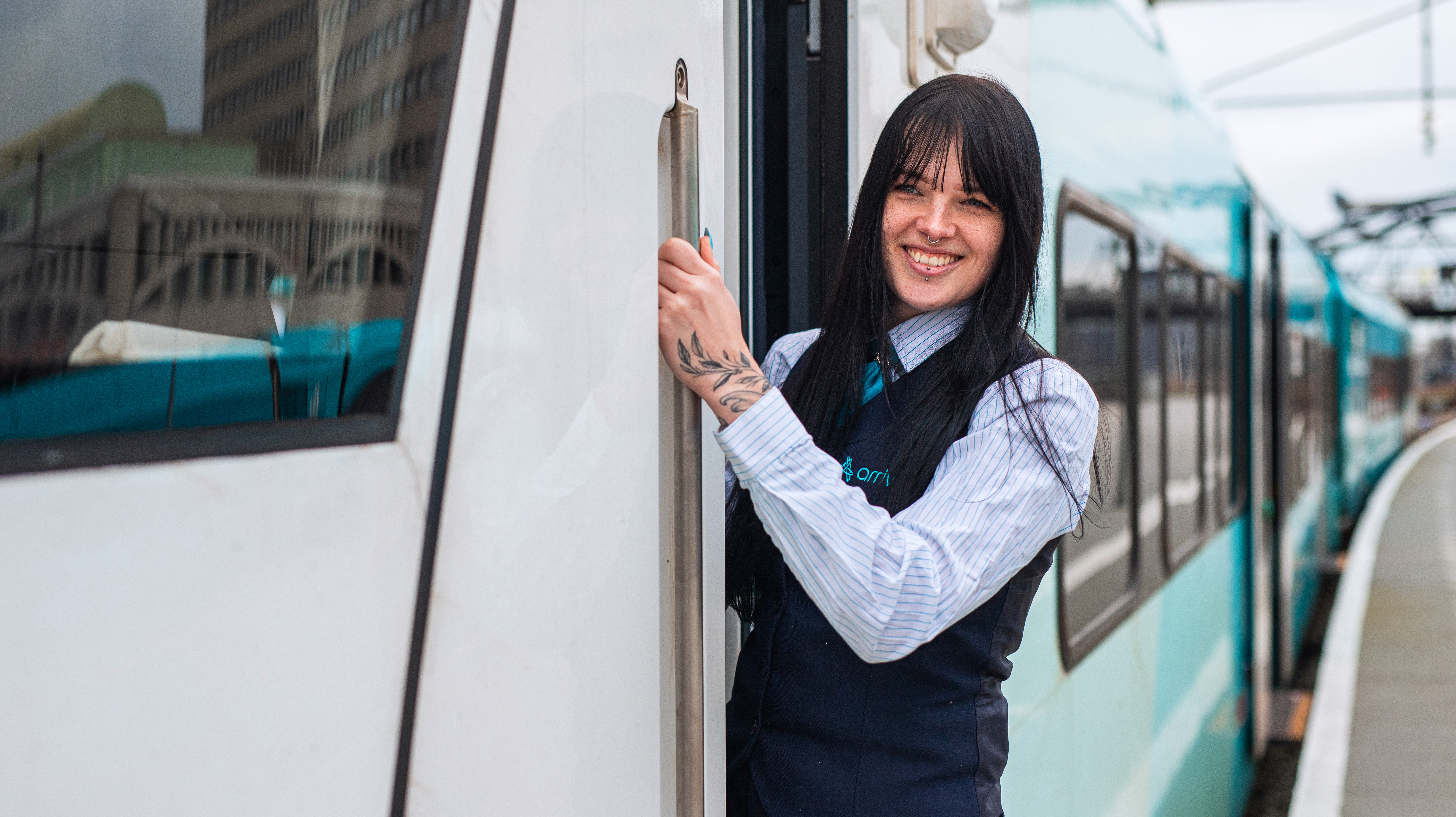 Vrouwelijke machinist staat in de deur van een Arrivatrein en lacht 