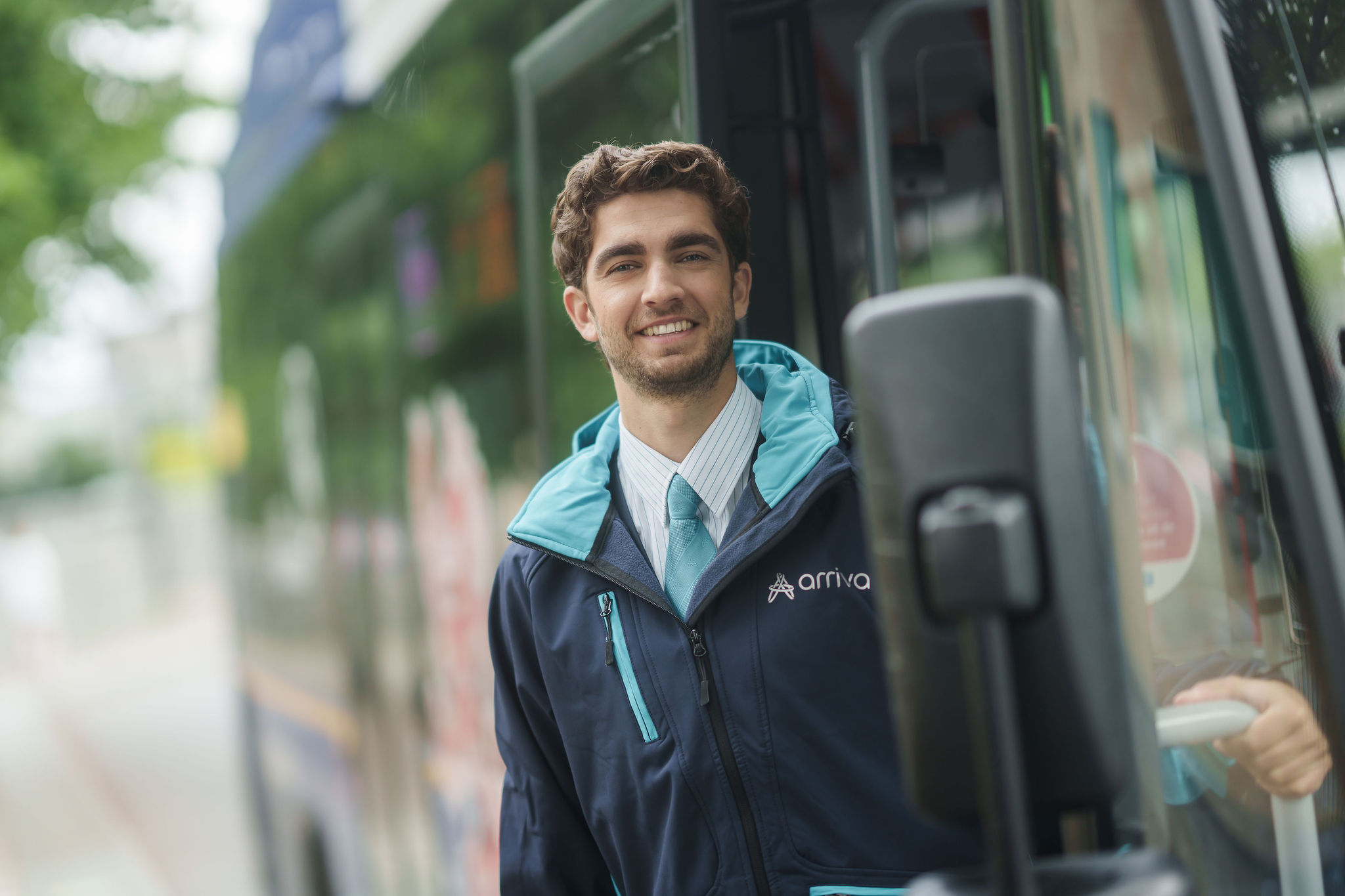 Buschauffeur van Arriva leunt uit zijn bus en lacht.