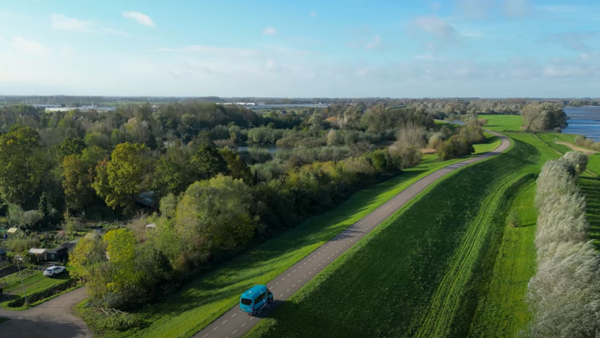 Filmstill van een bovenaanzicht van en weg op een dijk met daarop een groene Arriva-buurtbus. Filmstill van een bovenaanzicht van en weg op een dijk met daarop een groene Arriva-buurtbus.