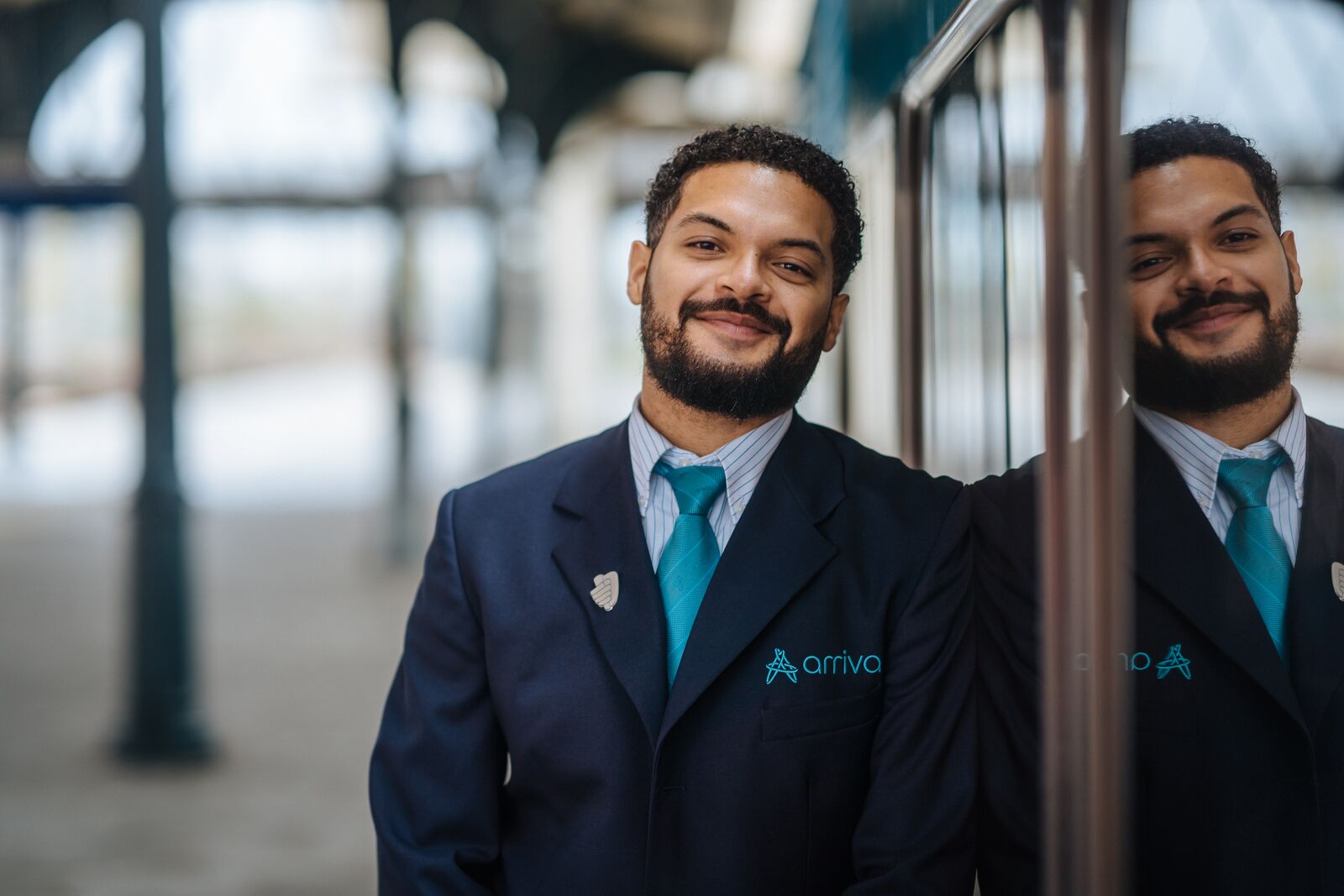 Mannelijke conducteur met donker haar en een baardje leunt tegen de zijkant van een Arriva-trein.