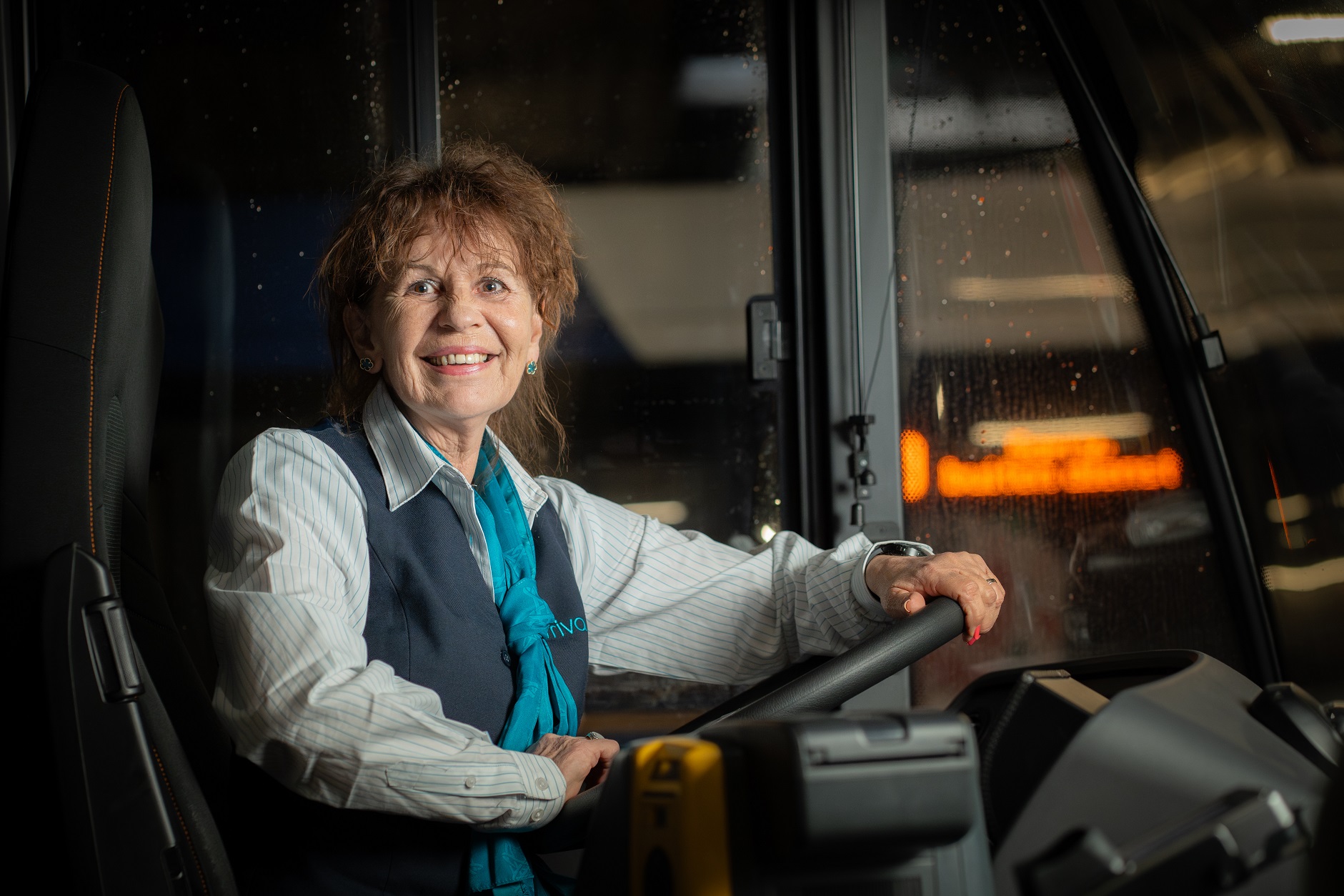 Buschauffeur Marion zit in haar Arriva-uniform lachend achter het stuur van een bus.