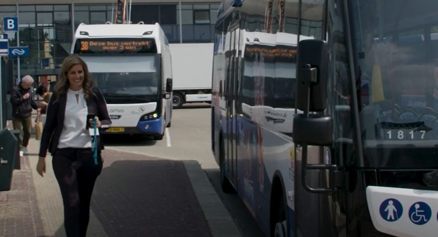 Een vrouw loopt langs een Arriva bus. Op de achtergrond staat nog een bus.
