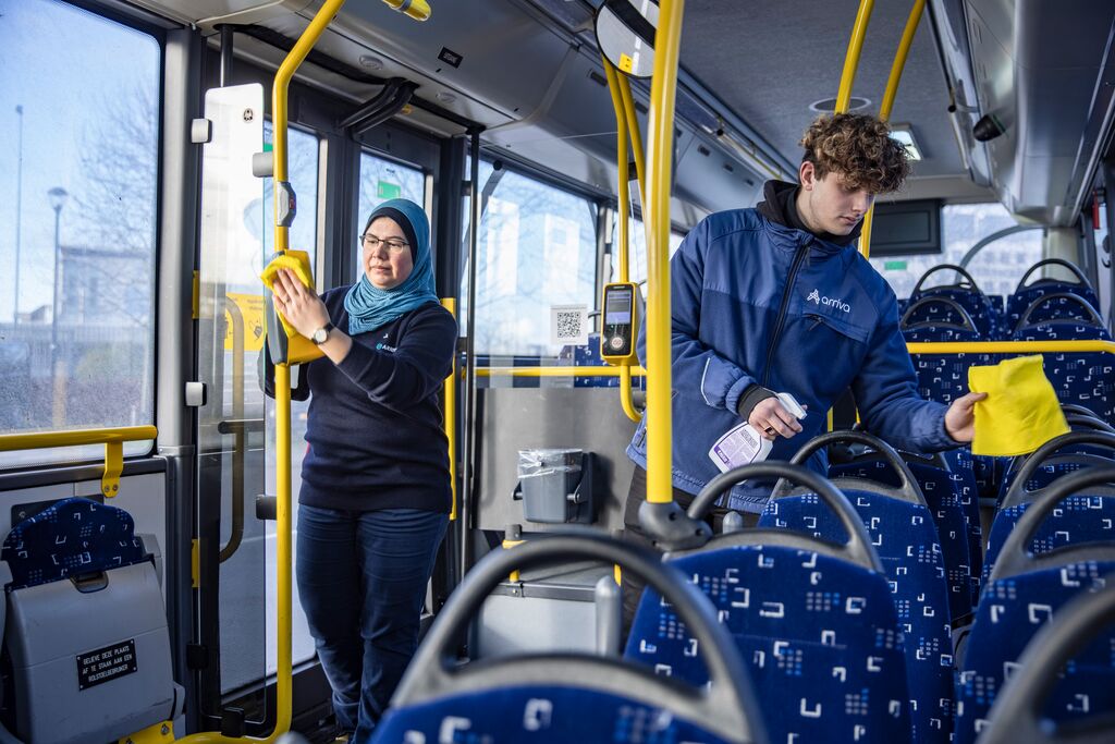 Twee service medewerkers, een jongen en een vrouw, zijn bezig met schoonmaken in een Arriva-bus.